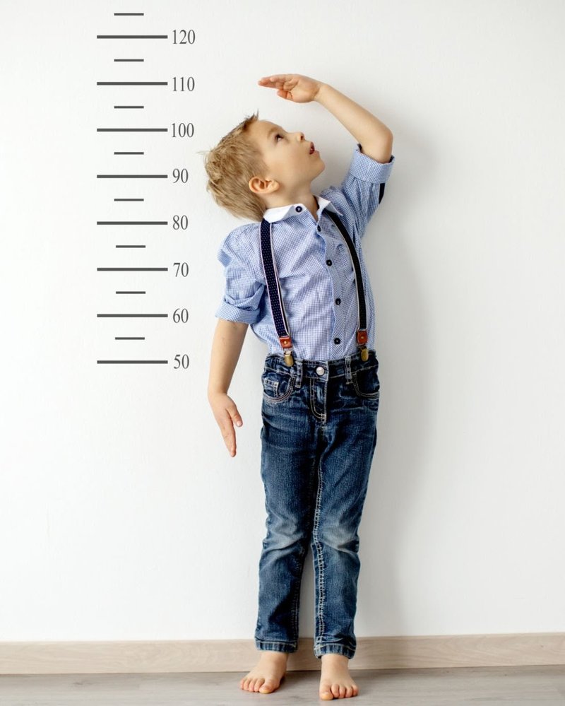Young boy in suspenders measuring his height against a wall ruler